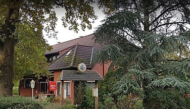Ein älteres Haus umgeben von verschiedenen Bäumen am Langholter Meer.