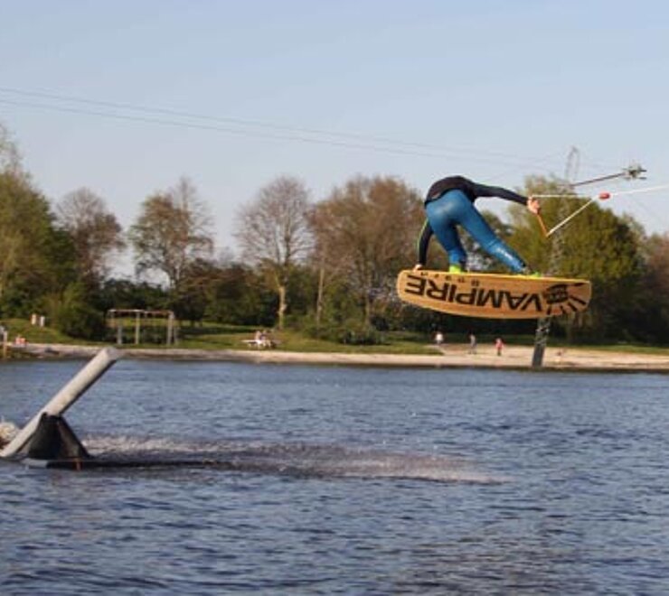 Auf dem Idasee spring ein Wassersportler über einen Metallpfahl der inmitten des Sees als Sprungschanze dient. 