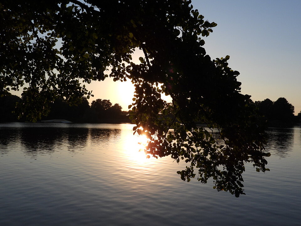 Hellorangener Sonnenuntergang am Idasee. Links und rechts befinden sich Bäume die den See umkreisen. 