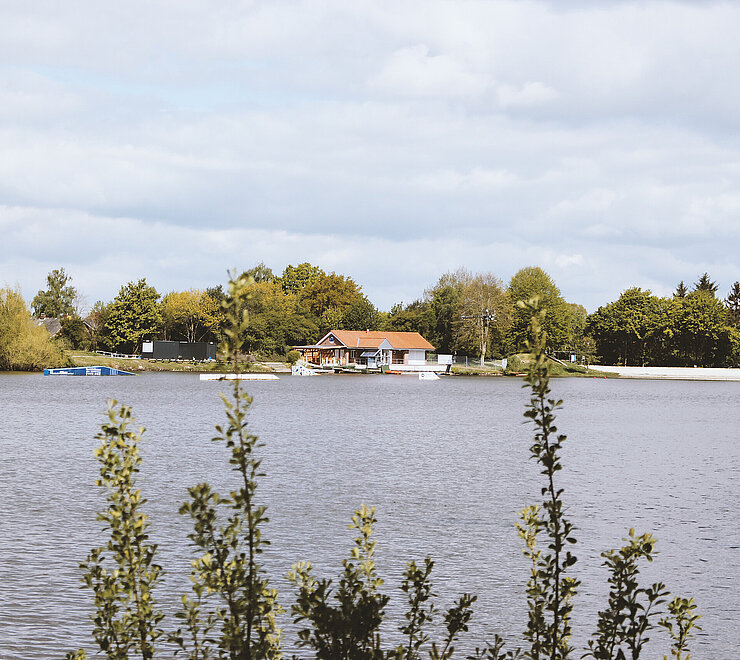 Blick auf den Idasee. Im Hintergrund vom See steht das Zentrum der Wasserskianlage. 