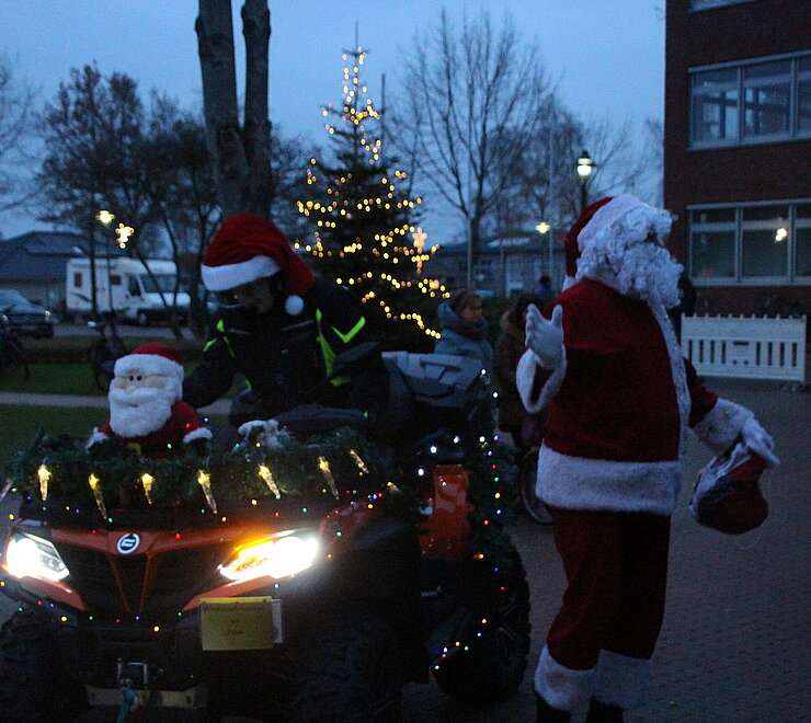 Weihnachtselfe und der Weihnachtsmann stehen mit einem geschmückten Quad vor dem Rathaus. Um sie herum stehen Eltern mit ihren Kindern. 